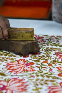 A carved wooden block being struck onto a length of cotton by hand