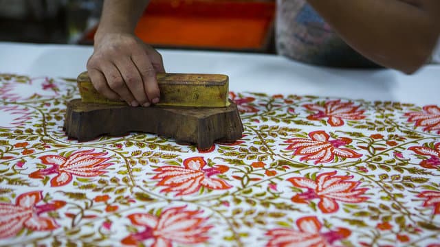 A carved wooden block being struck onto a length of cotton by hand