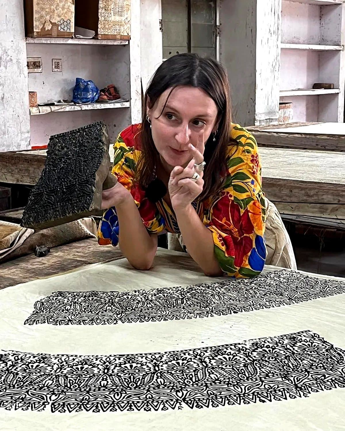 Camille at the printing table in Rajasthan, holding one of the hand-carved wooden blocks over a length of freshly printed cloth