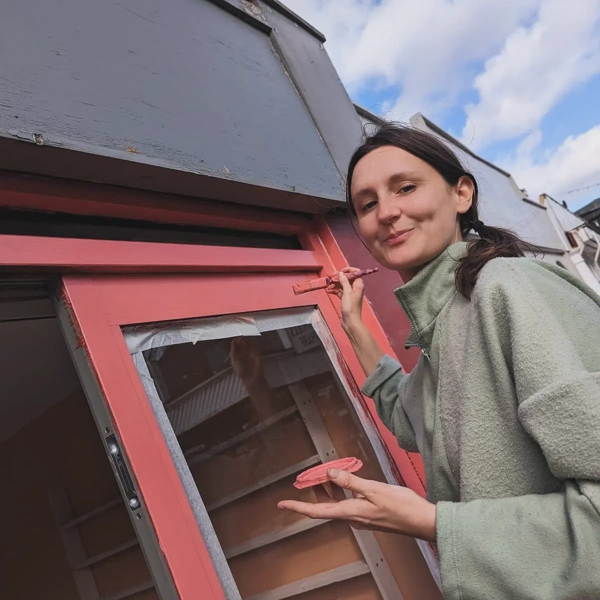 Camille painting the shopfront window frame coral pink by hand